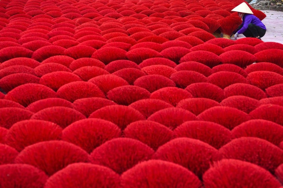 A person kneels down, placing a bundle of bright-red incense sticks among many other bundles.