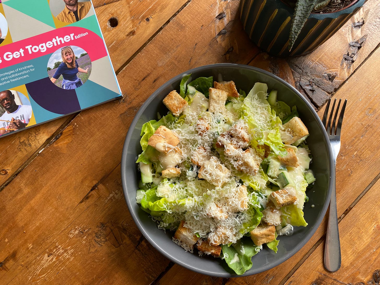 bowl of salad with grated cheese, lettuce, croutons and dressing in a grey bowl on a wooden table. A magazine is placed next to it.