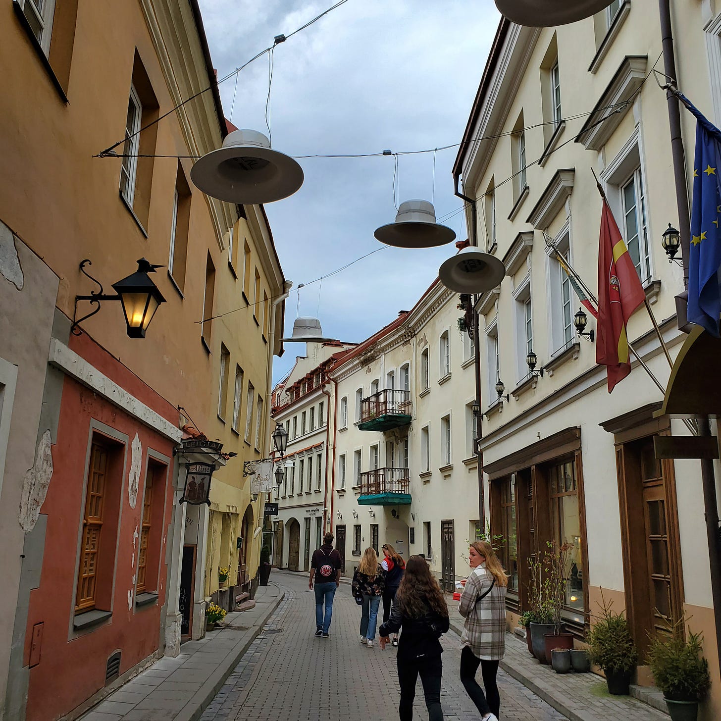 A small European city streets over which decorate hats hang on wires.