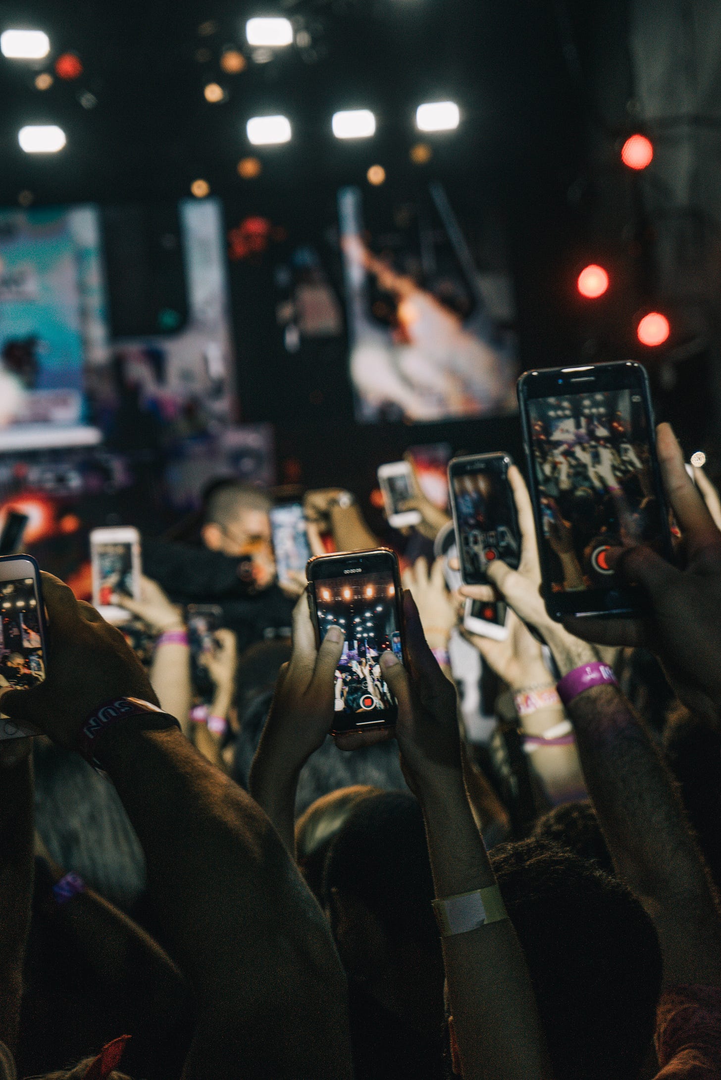 Photo of a crowd at a gig holding up their mobile phones to film the concert. You can see multiple screens showing what they are filming. Photo by Gian Cescon on Unsplash