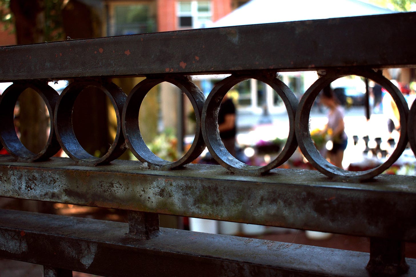 Photograph of an old gate, through which we see people at Vancouver Farmer's Market buying colorful flowers.