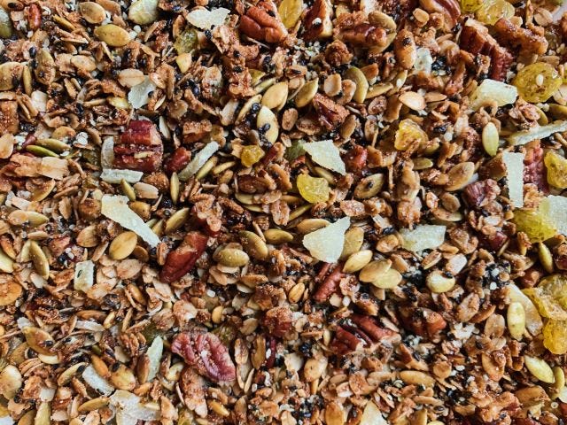 Close up texture of granola, with oats, pumpkin seeds, candied ginger, and black sesame visible