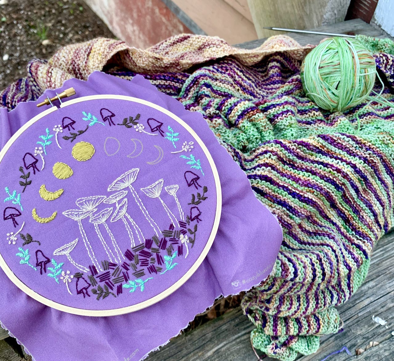 An embroider hoop  of mushrooms and moons on top of a striped shawl