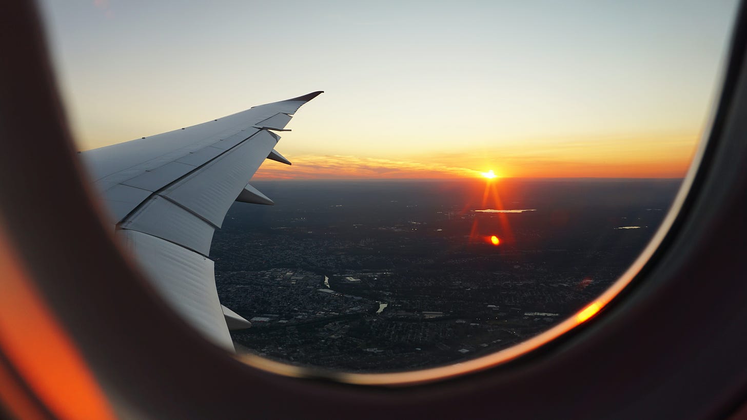 View out of an airplane window of a low sunset over a city with the plane wing in view as well.