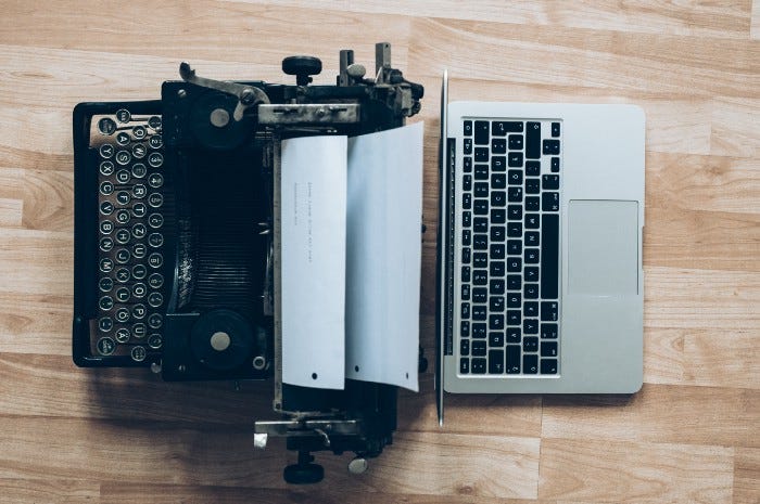 An Antique typewriter is on the left, and a modern Apple laptop is on the right.