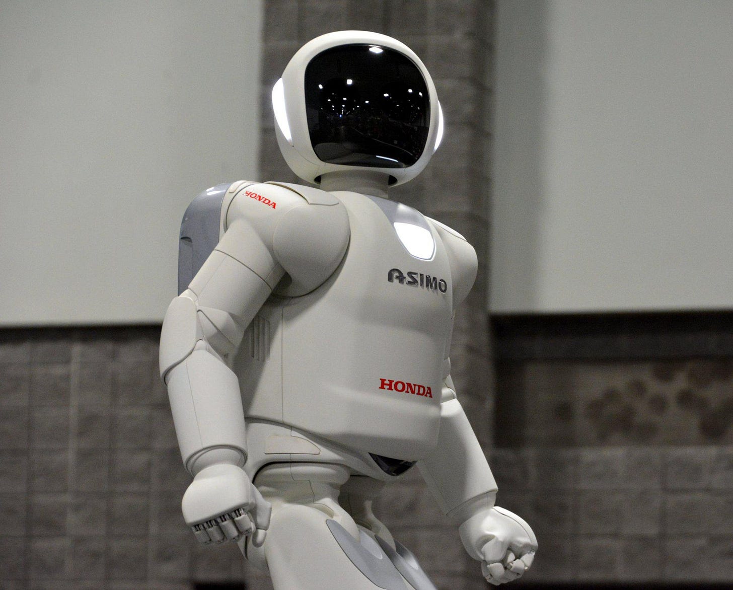 A white humanoid robot with a black helmet stands facing the camera