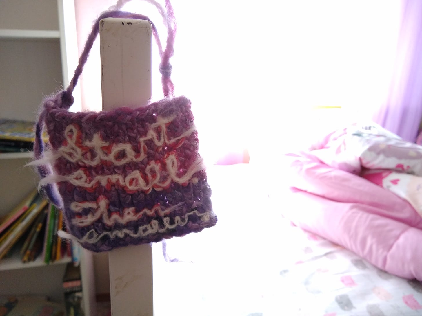 A pink and purple swatch with "Start small. Then smaller." felted onto it, hanging from a kid's bedpost.