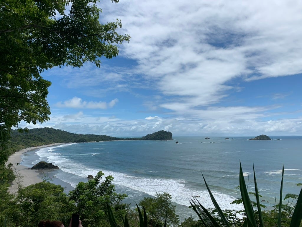 A beach in Costa Rica at midday, with the tide coming in and clouds in the sky.