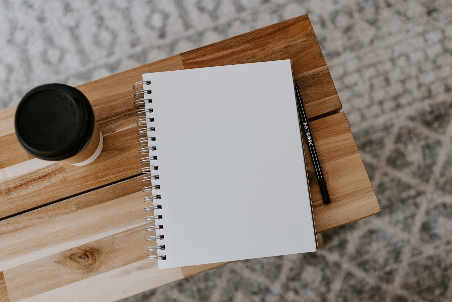 A notebook, pen and coffee cup sitting on a wooden bench