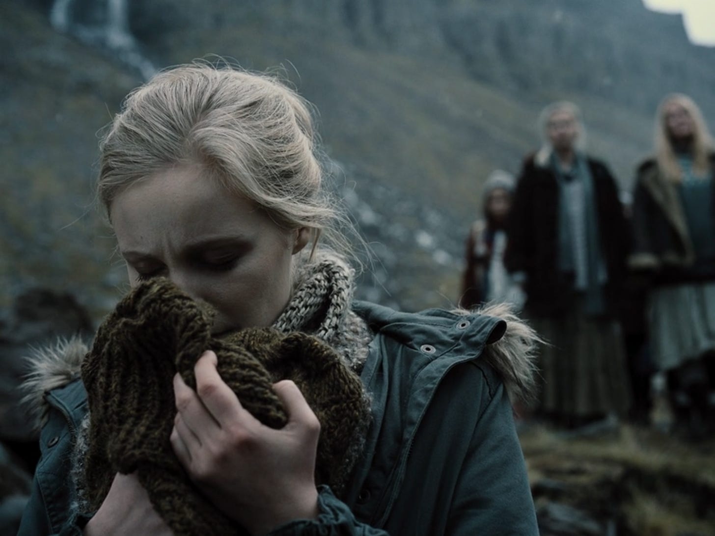 A blonde Icelandic woman clutches a brown cable-knit sweater and smells it while standing near the ocean in 'Zack Snyder's Justice League'