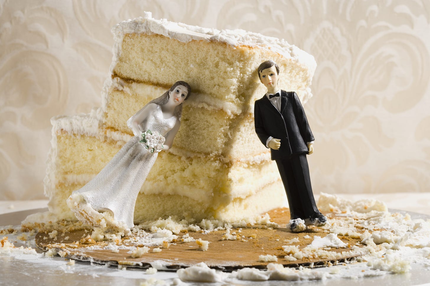 Plastic bride and groom figurines leaning against a slice of wedding cake