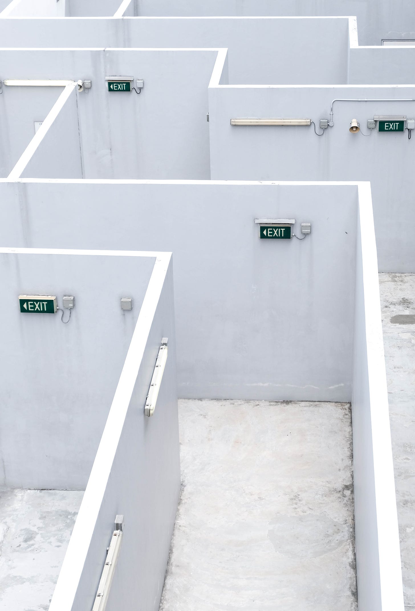 Photo of a maze with white walls and several green exit signs