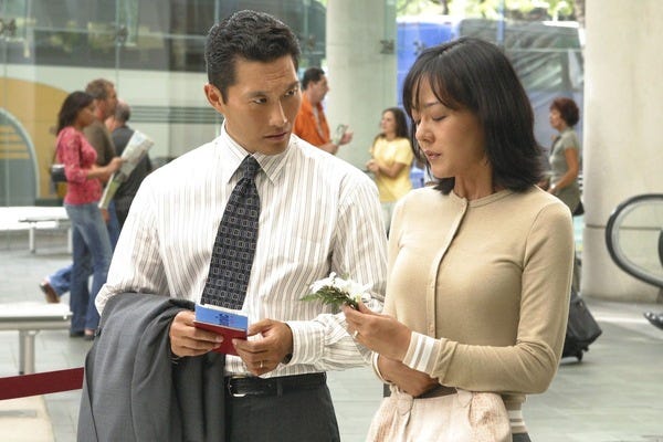 Jin-Soo Kwon (Daniel Dae Kim) and Sun-Hwa Kwon (Yunjin Kim) confer in an airport concourse. Jin holds their tickets. Sun holds a flower.