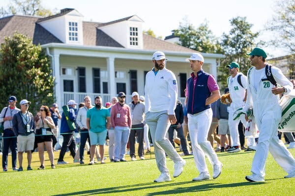 Two golfers — Dustin Johnson and Billy Horschel — walk down a fairway with their caddies, with fans lined up along the rope behind them.