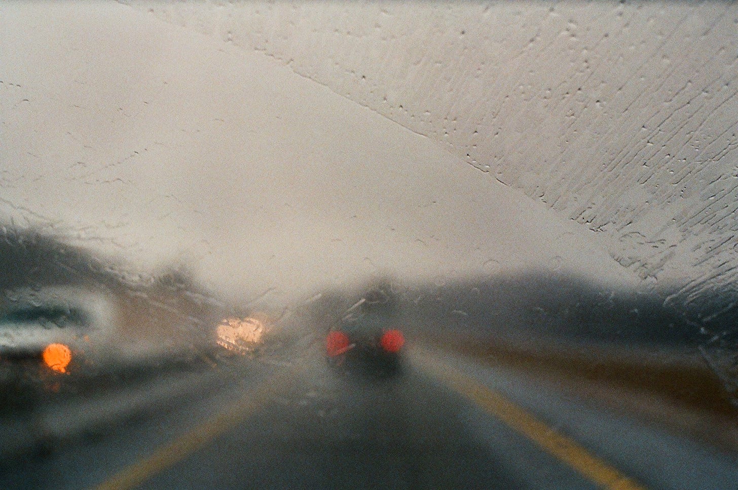 Blurred car taillights through a rain soaked windshield.