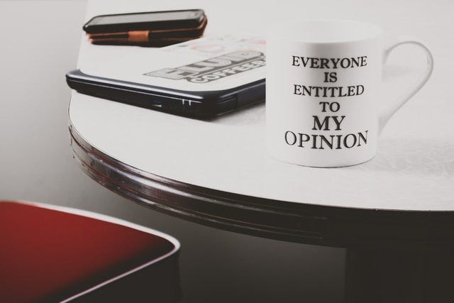Image of a mug on a table with a phone and a keyboard, with a slogan that says: "Everyone is entitled to my opinion", used to illustrate post.