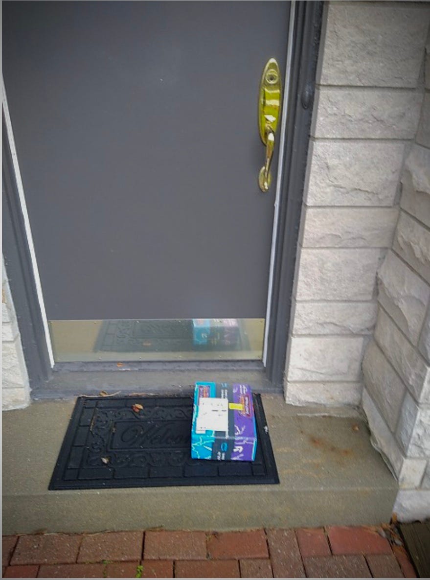 An Amazon package sits on a welcome mat on a front stoop in front of a door.
