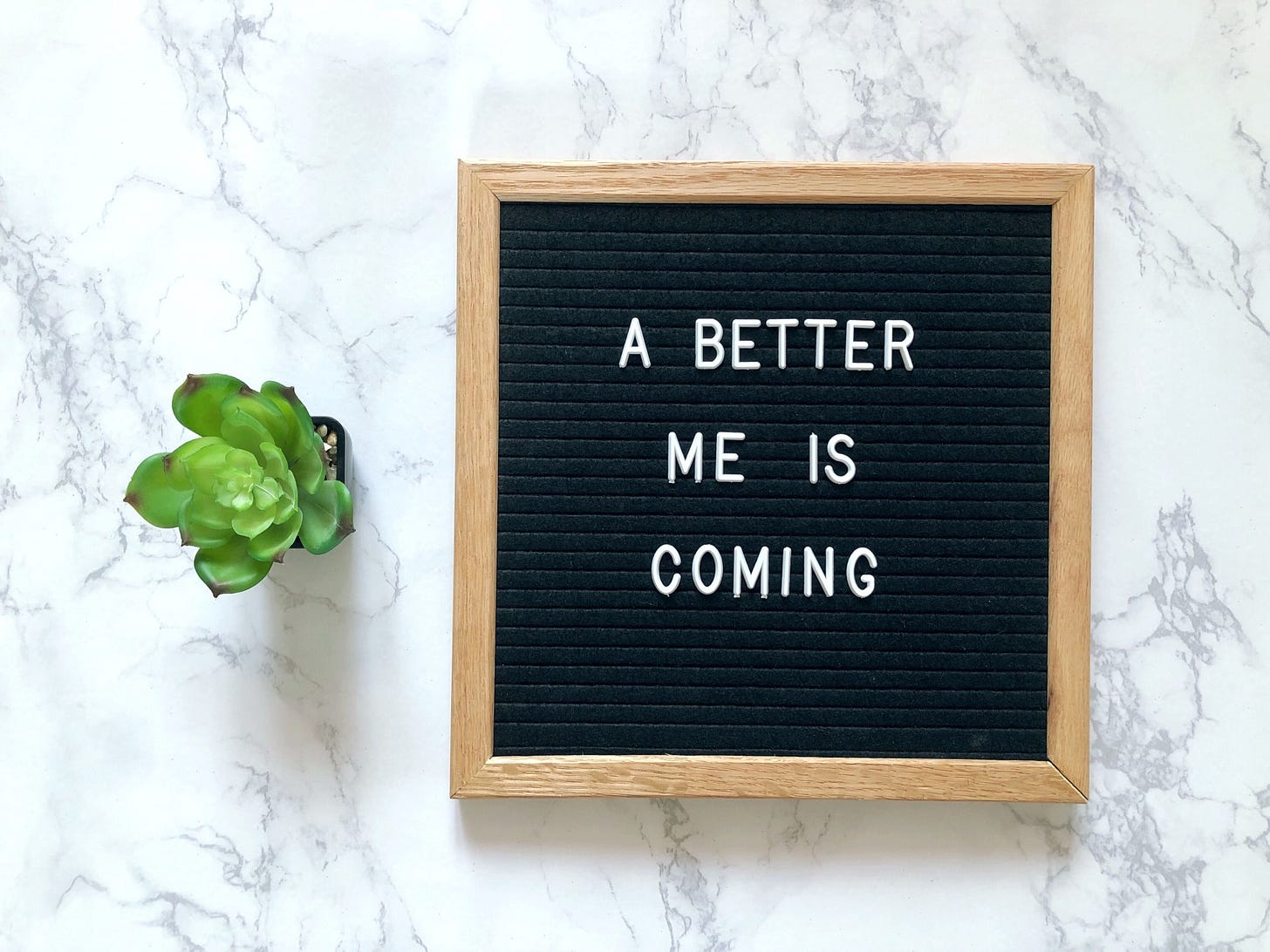 A sign reading ‘A better me’ sits against a white background. A small plant sits beside it.