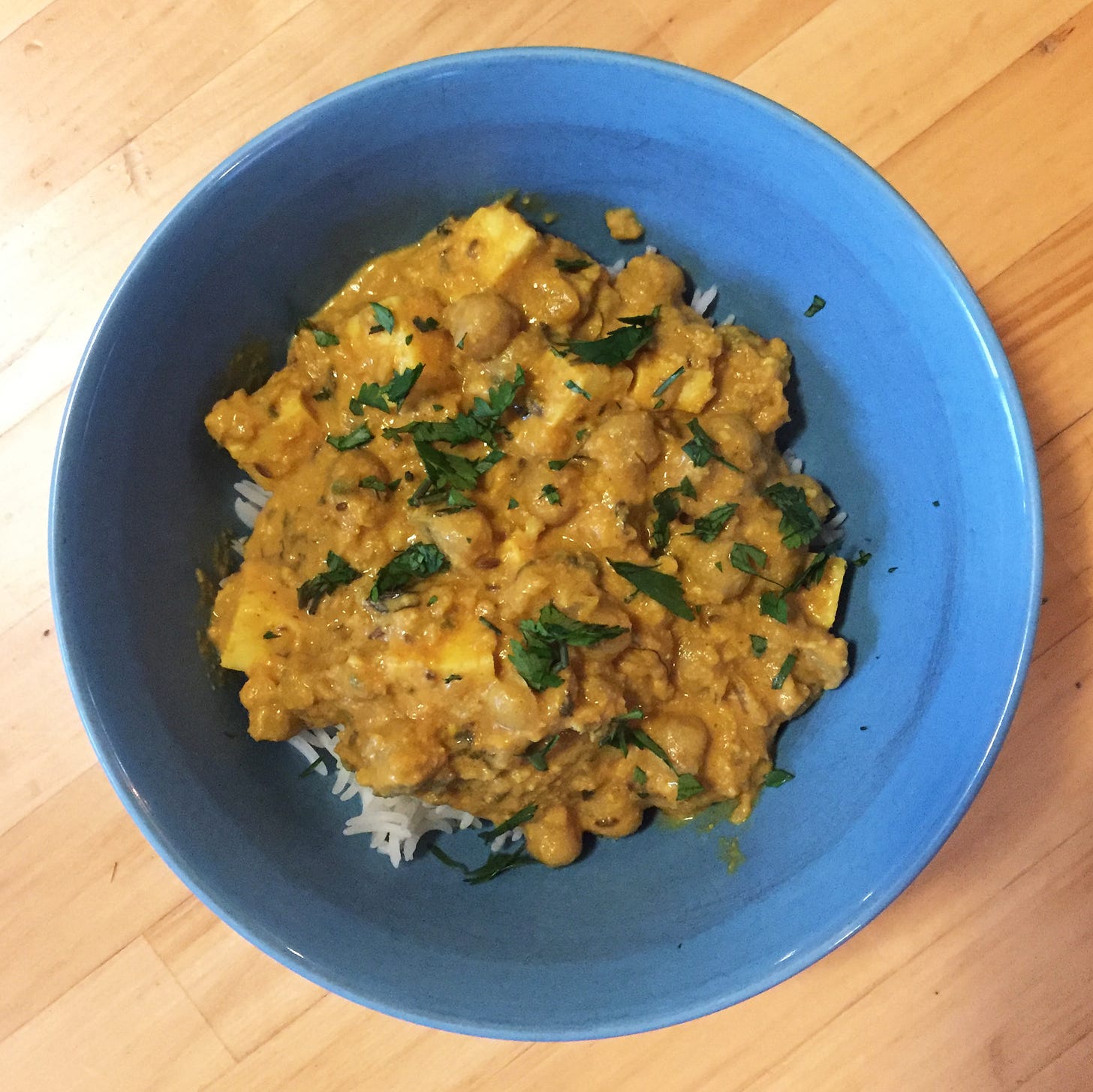 A blue bowl full of basmati rice and a thick yellow curry with chickpeas and paneer. Cilantro is sprinkled over the top.