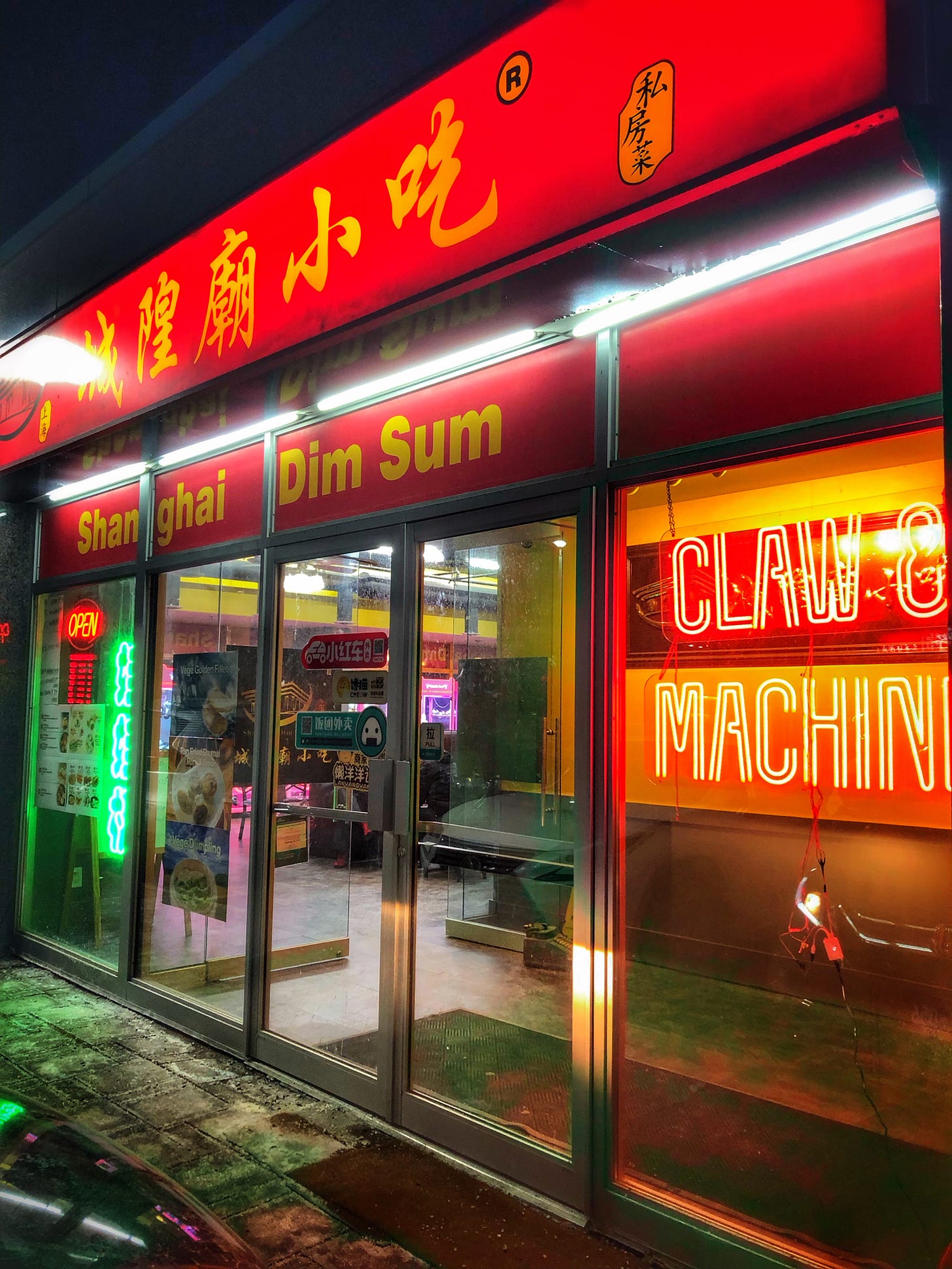 The exterior of the restaurant Shanghai Dim Sum. There is a neon sign in the window that reads "Claw Machine." Through the windows a row of arcade claw machines is visible. 