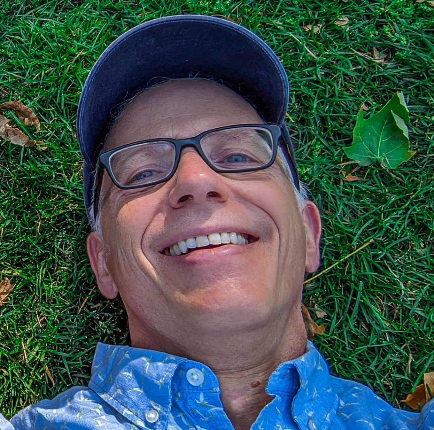 A smiling Michael laying in green grass as he looks up at the camera. 