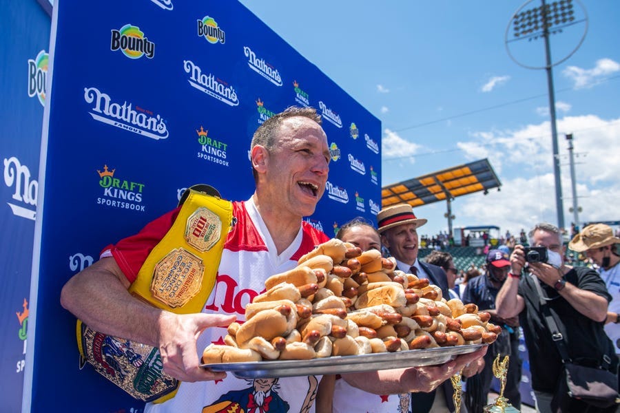 Winners Joey Chestnut and Michelle Lesco, obscured behind hot dogs, pose at the Nathan's Famous Fourth of July International Hot Dog-Eating Contest.