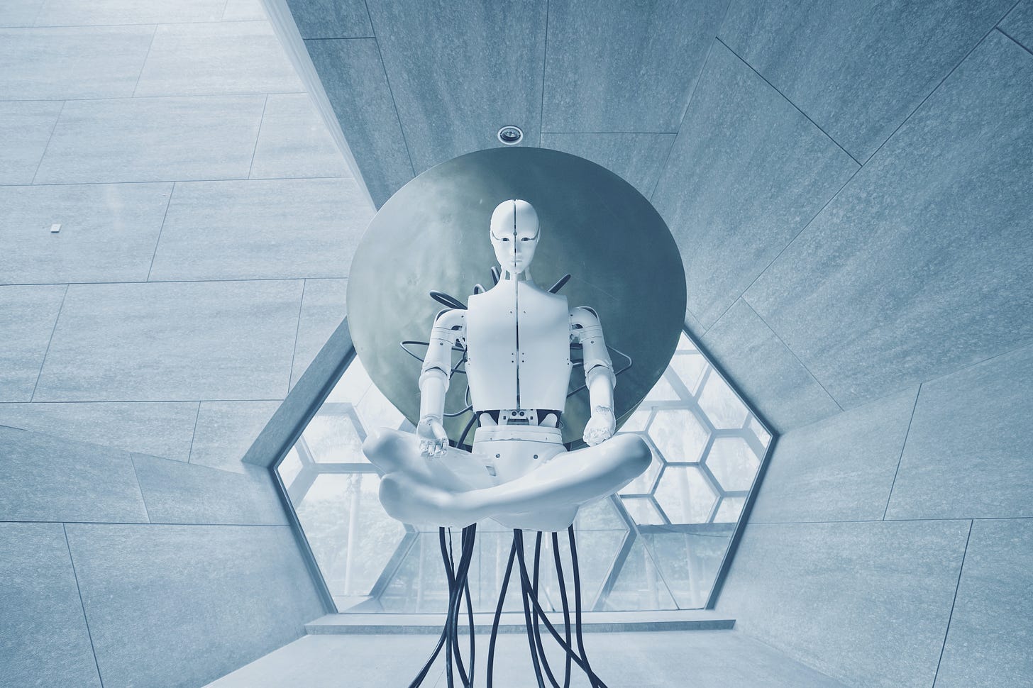 A futuristic white and metal laboratory. In the middle is a human/ robot in a pod and there are wires connected underneath.