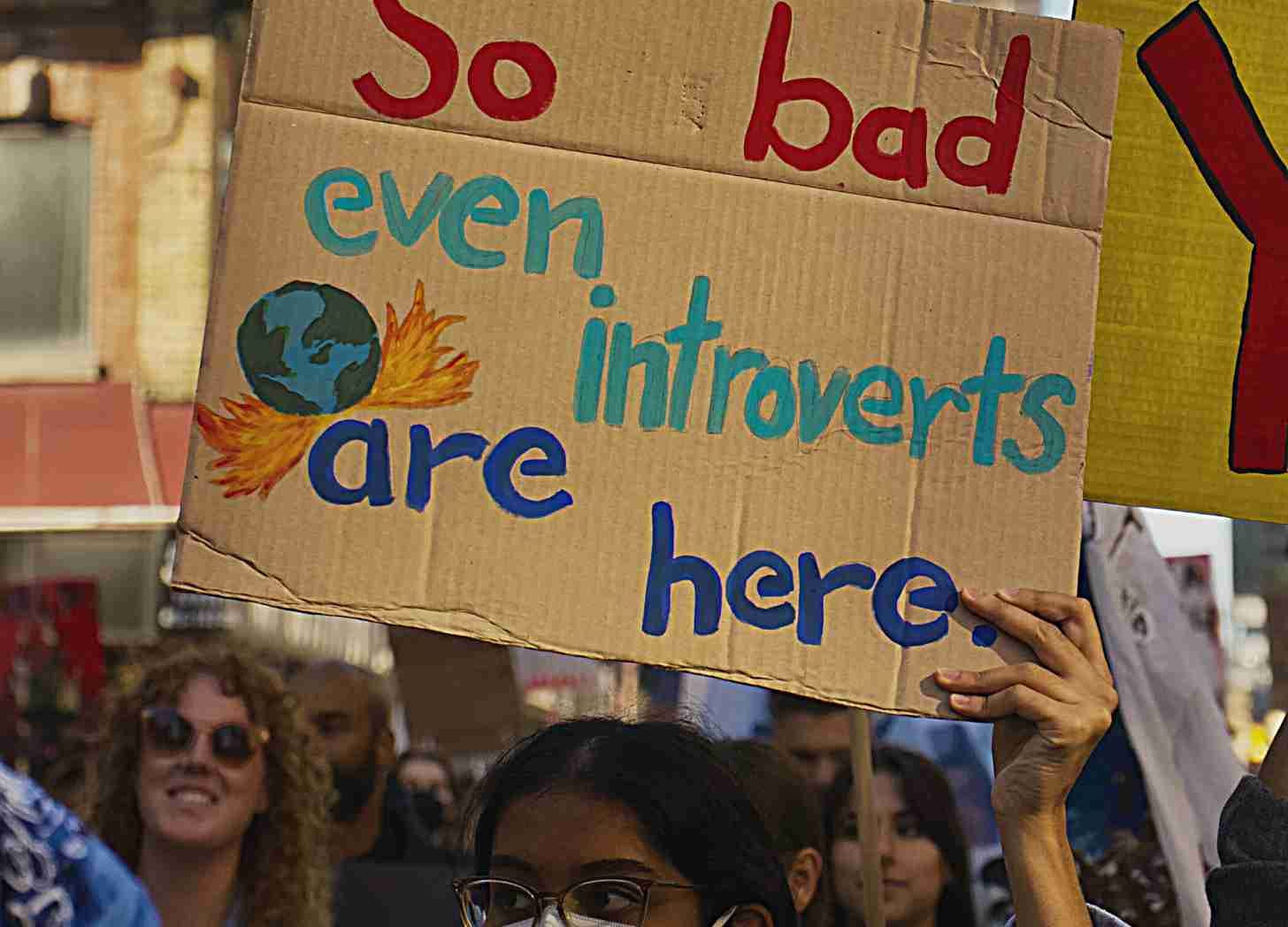 A climate protestor holds a cardboard sign that reads "So bad even intorverts are here