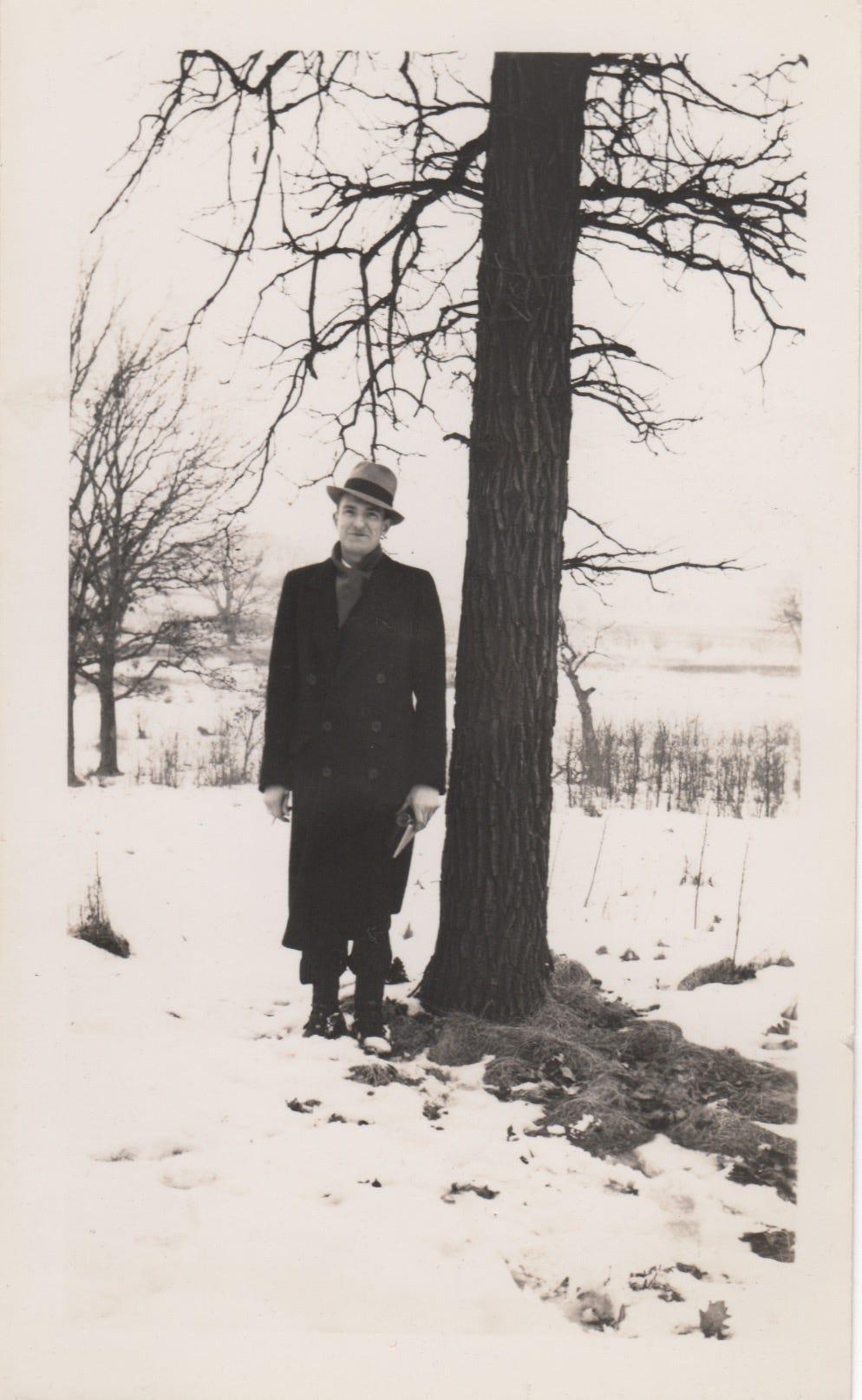 Photo of E Lowell Kammerer standing next to a tree trunk. There is snow on the ground, and the landscape is very wintery.