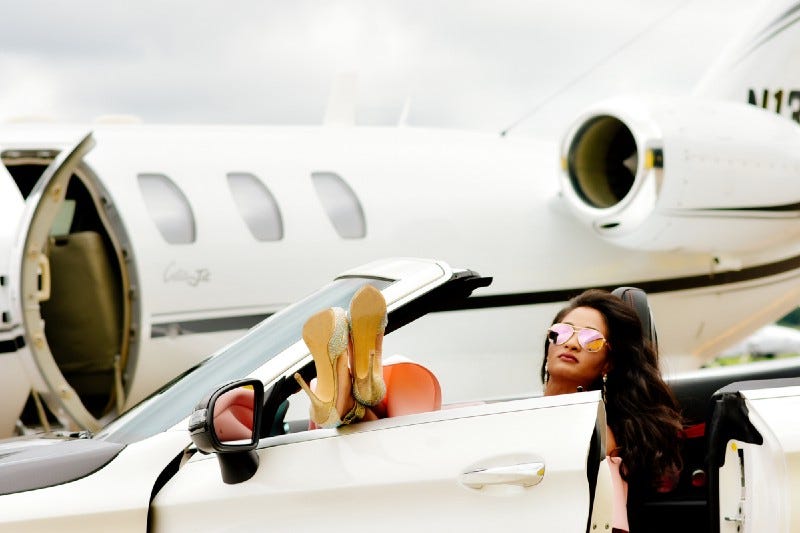 A wealthy women in a convertible beside a private jet