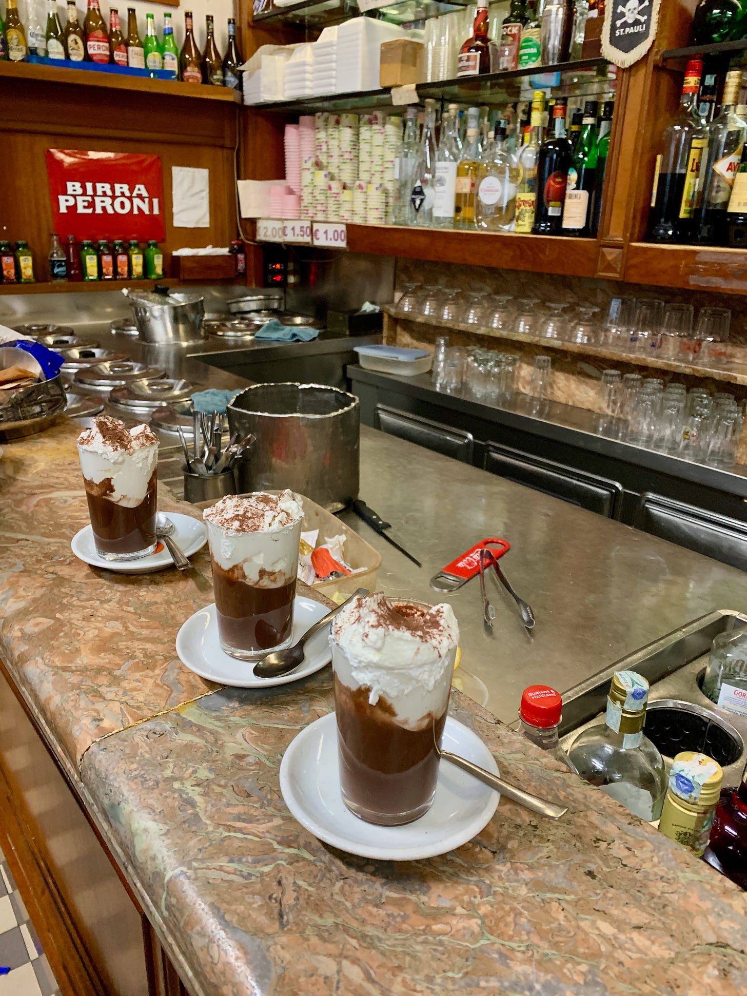 3 hot chocolates with whipped cream on the bar at Bar San Calisto in Rome