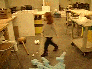 A small red headed girl walks up to a stool, climbs on top of it, and starts playing with styrofoam packing peanuts.