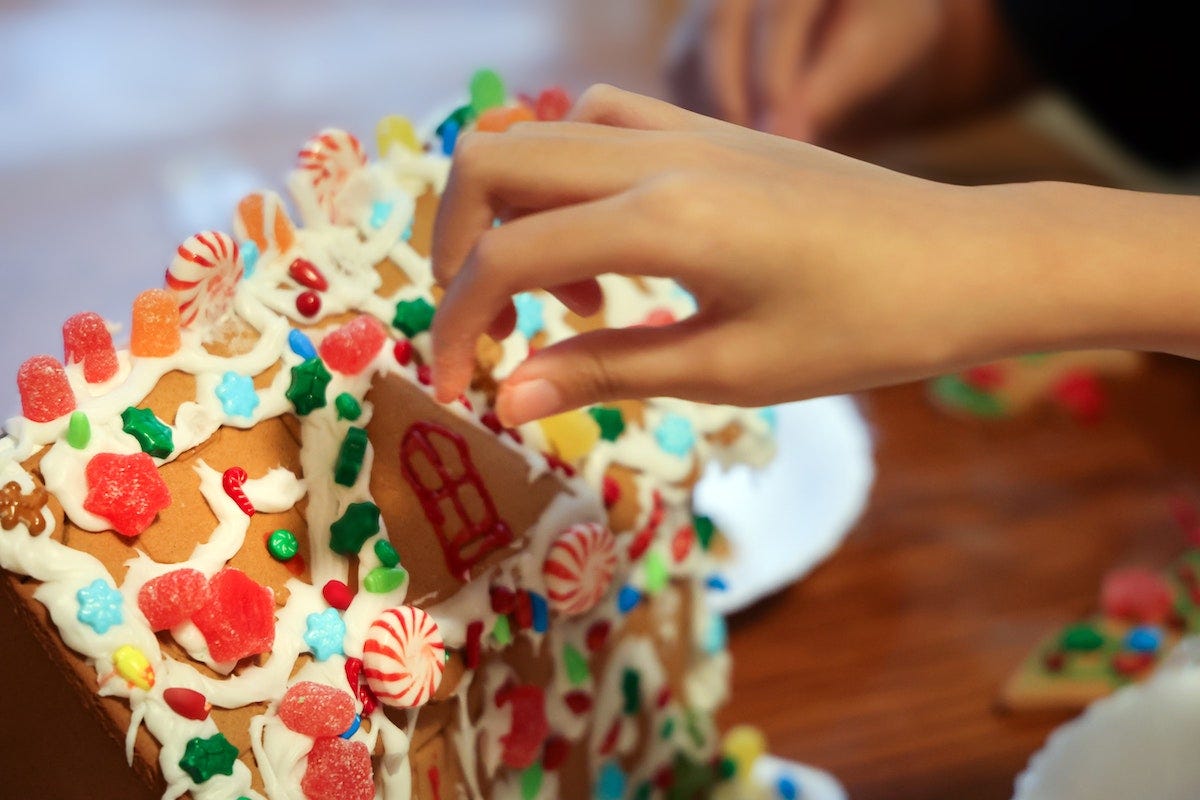 Hand reaching out to take a piece of a homemade gingerbread cottage on a table.