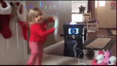 GIF: A toddler girl dances with a karaoke machine in front of Christmas stockings