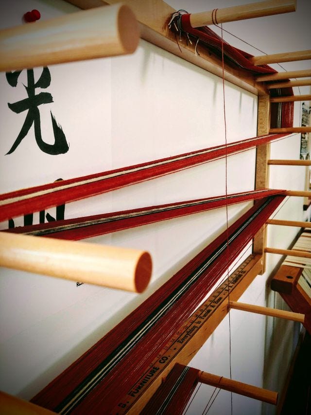 Photograph of orange, white, and navy coloured thread being wound on a pegged warping board to create a warp chain. 