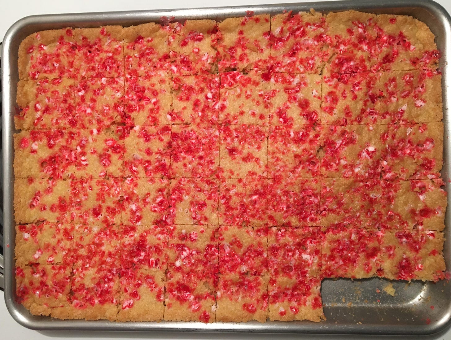 A pan of bar cookies with crushed peppermint candy on top, cut into squares, with the bottom right two cookies missing. 