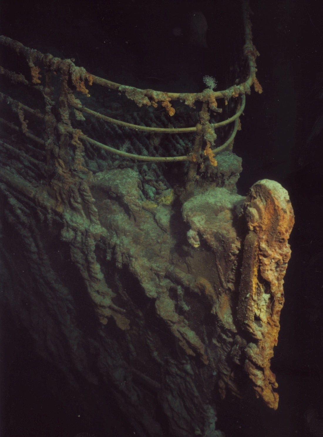 A closeup of the degraded bow of the wreck of the Titanic. It is illuminated from the front, and is a muddy brown.
