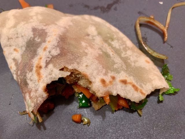 A pancake folded around green and orange vegetables, with a large bite taken out of it