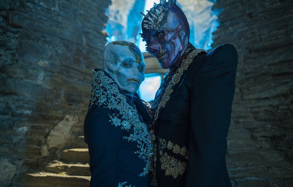 This image shows the character of Azure (played by Rochenda Sandall) standing on the left and the character of Swarm (played by Sam Spruell) standing on the right looking directly into camera.