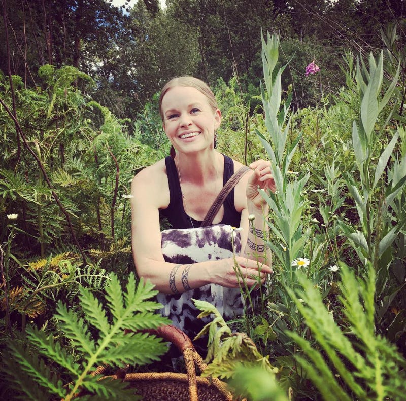 Photo of me sitting in a field of tansy and mugwort with a black tank top and long skirt.