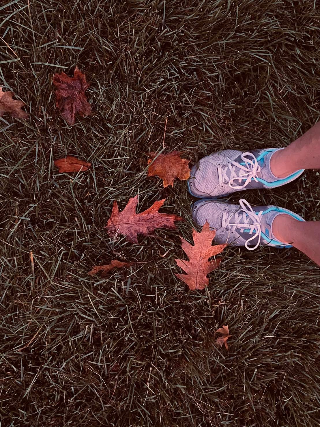 blue and gray sneakers on dark green grass with brown fallen leaves scattered about