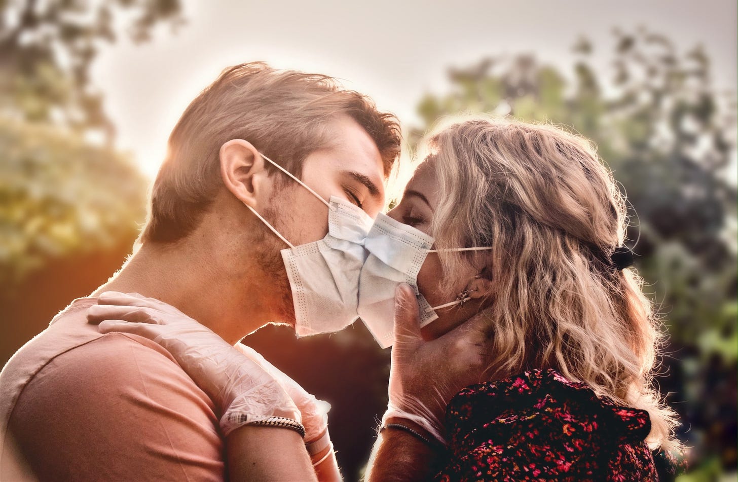 A couple (in masks) embrace for a kiss in the afternoon light.