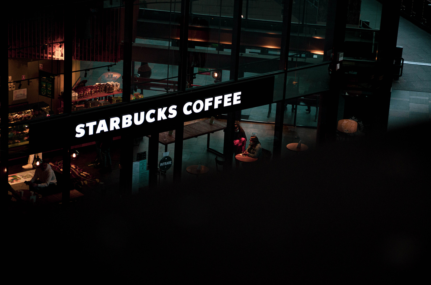 A brightly lit Starbucks cafe at night, with a dark blurred shape in the foreground