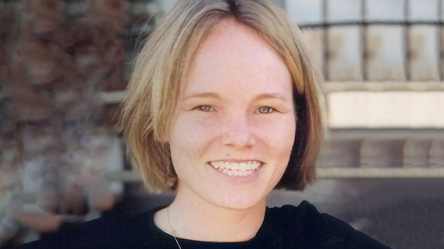 A blond white woman with medium length hair and a toothy grin