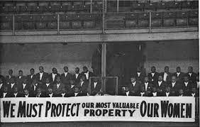 This image shows part of the audience at a Nation of Islam rally sometime in the early 1960s. The all-male attendees sit behind a large banner bearing the slogan "We Must Protect Our Most Valuable Property Our Women." This image shows part of the audience at a Nation of Islam rally sometime in the early 1960s. The all-male attendees sit behind a large banner bearing the slogan "We Must Protect Our Most Valuable Property Our Women."