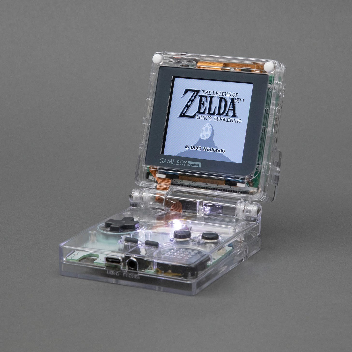 A picture of the Game Boy Pocket SP, a Game Boy Pocket handheld video game system in a clear plastic custom built folding case with a hinge between the screen and the controller, in the style of the Game Boy Advance SP.
