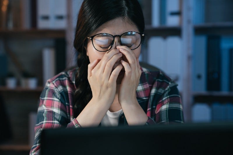 A tired-looking student sits in front of her laptop computer and rubs her eyes.