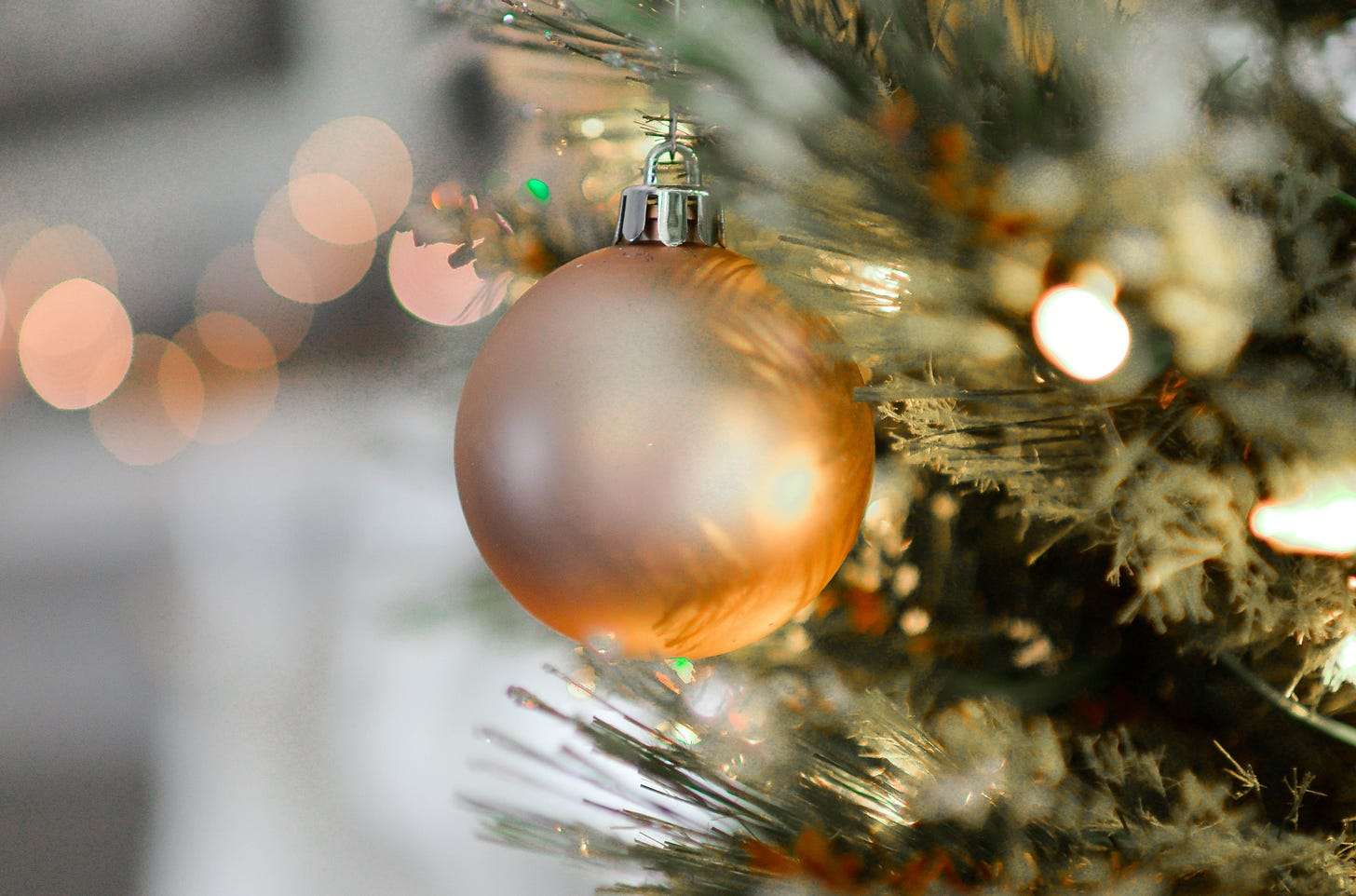 A gold Christmas bauble hangs on some greenery that also have twinkling lights festooned throughout.