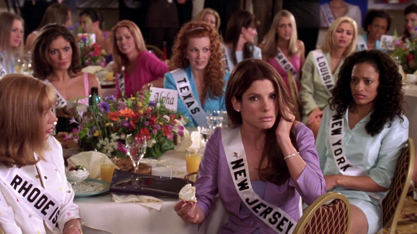 A group of Miss USA contestants wearing dresses and sashes sit around a breakfast table.