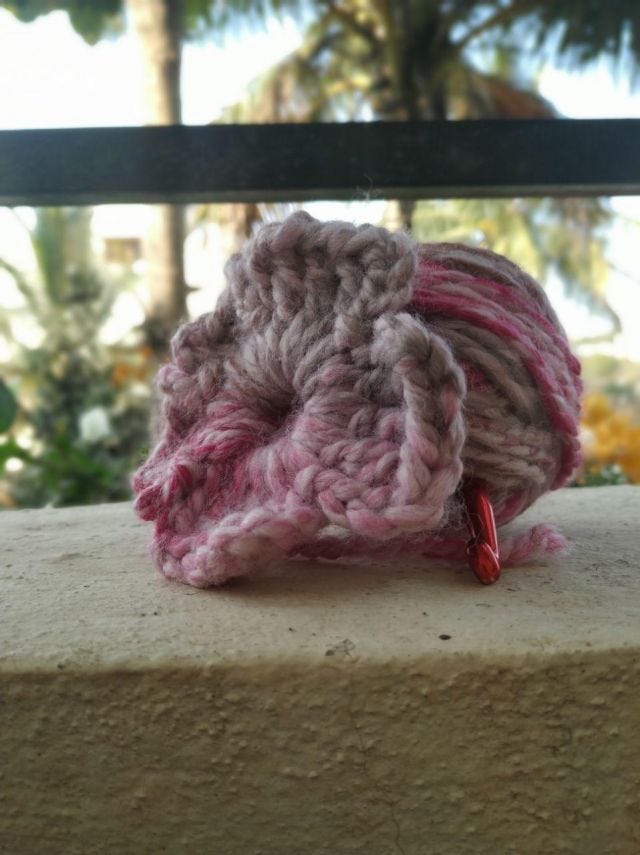 A crocheted pink and white flower with a ball of yarn next to it.